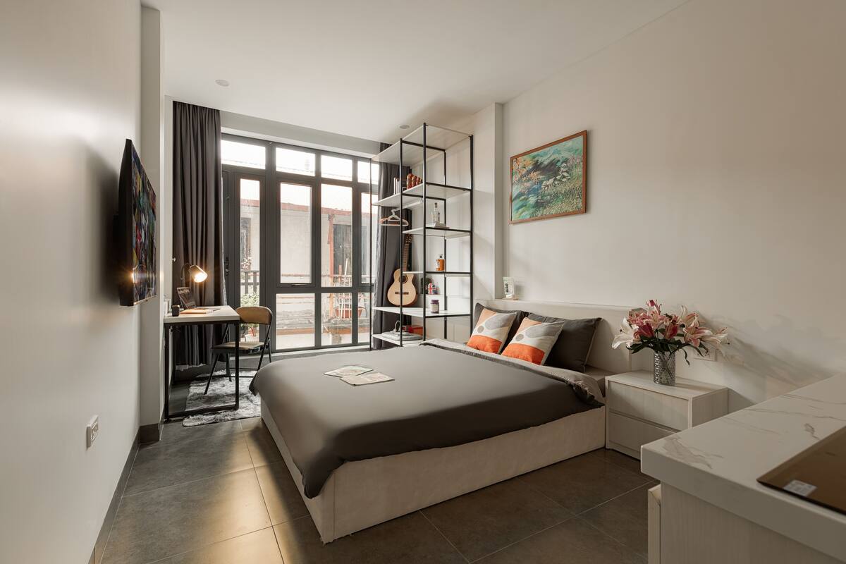 A modern bedroom with a large bed, a desk, and a bookshelf.