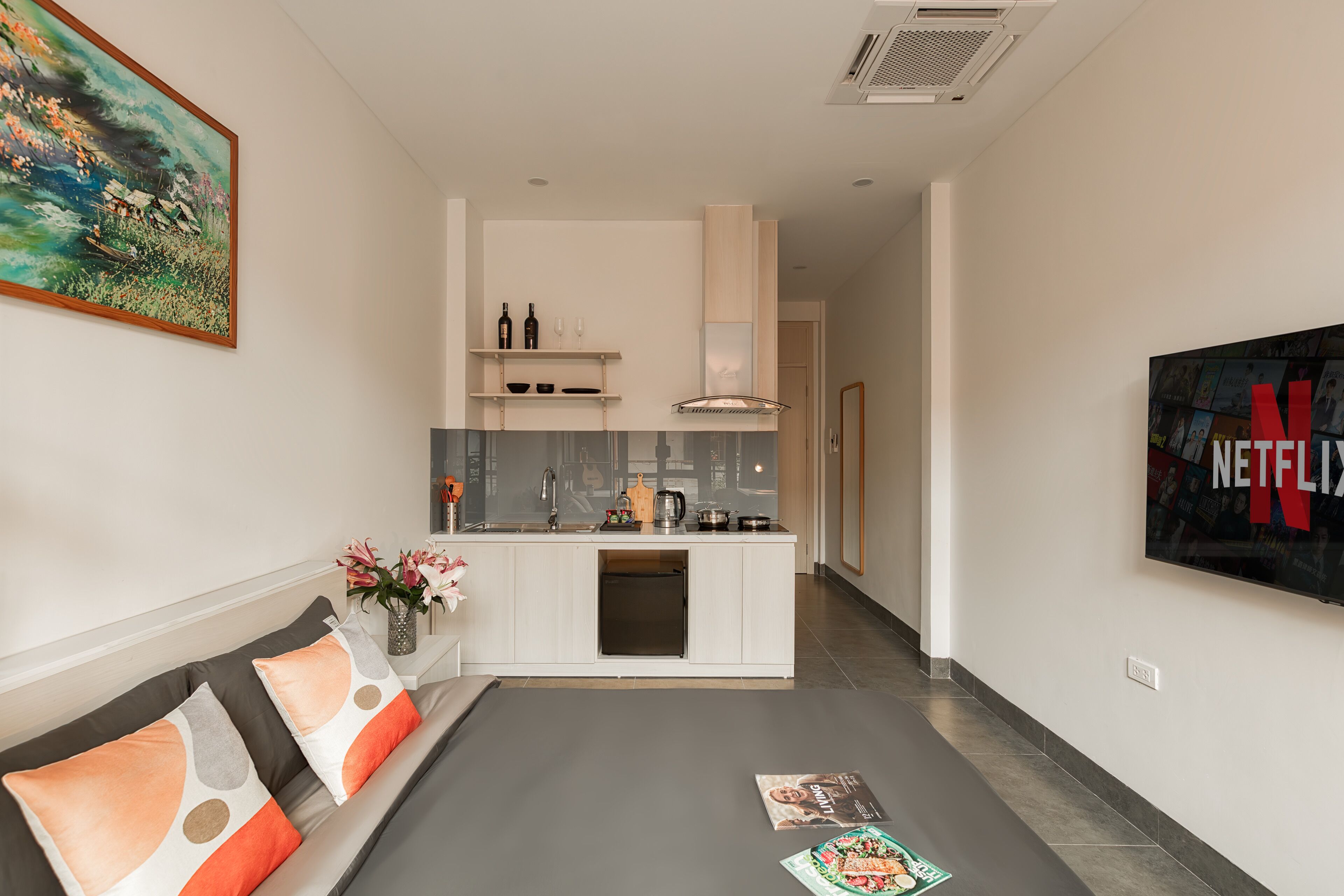 A modern living room with a grey sofa, a coffee table, and a kitchen area with white cabinets and a sink.