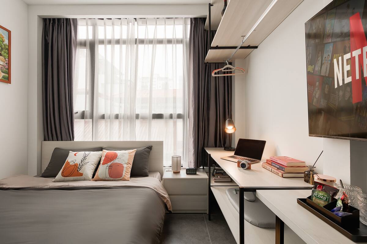 A modern hotel room with a bed, desk, and large window.