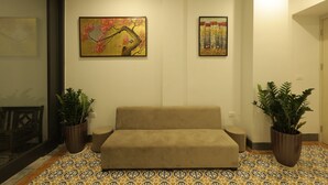 Un accogliente soggiorno con un divano beige, due piante in vaso e due quadri appesi al muro.