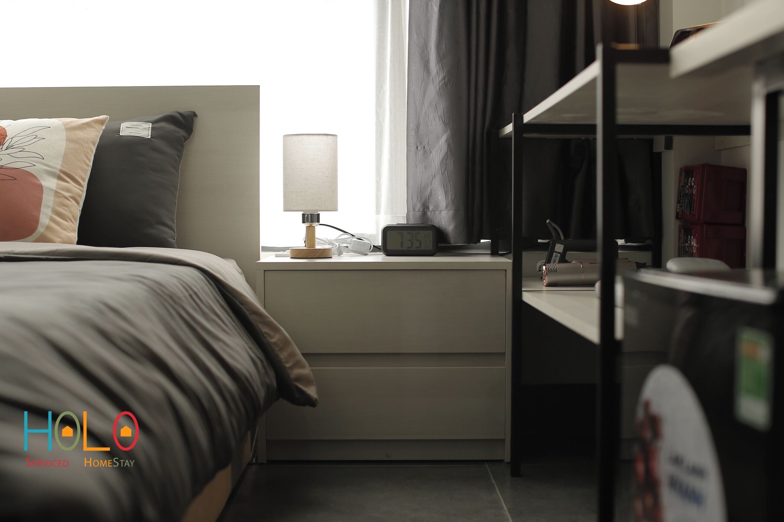 A hotel room with a bed, bedside table, lamp, clock, and a bunk bed.