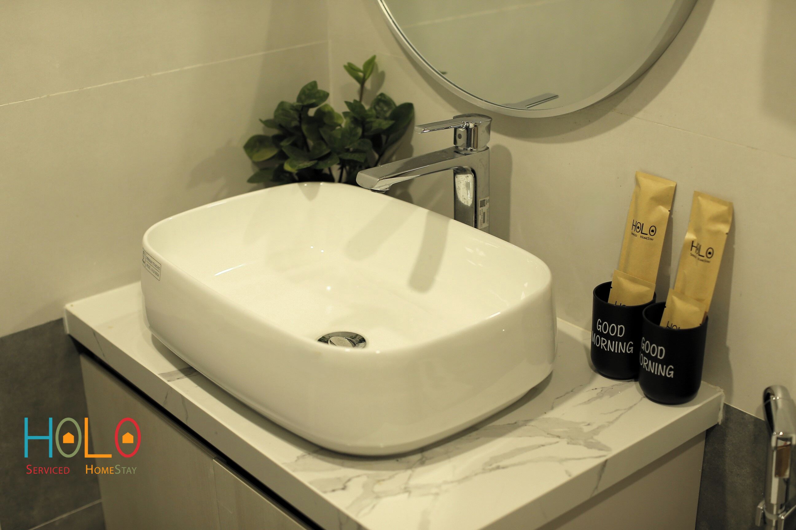 A bathroom with a white sink, a mirror, and two cups with 'Good Morning' written on them.