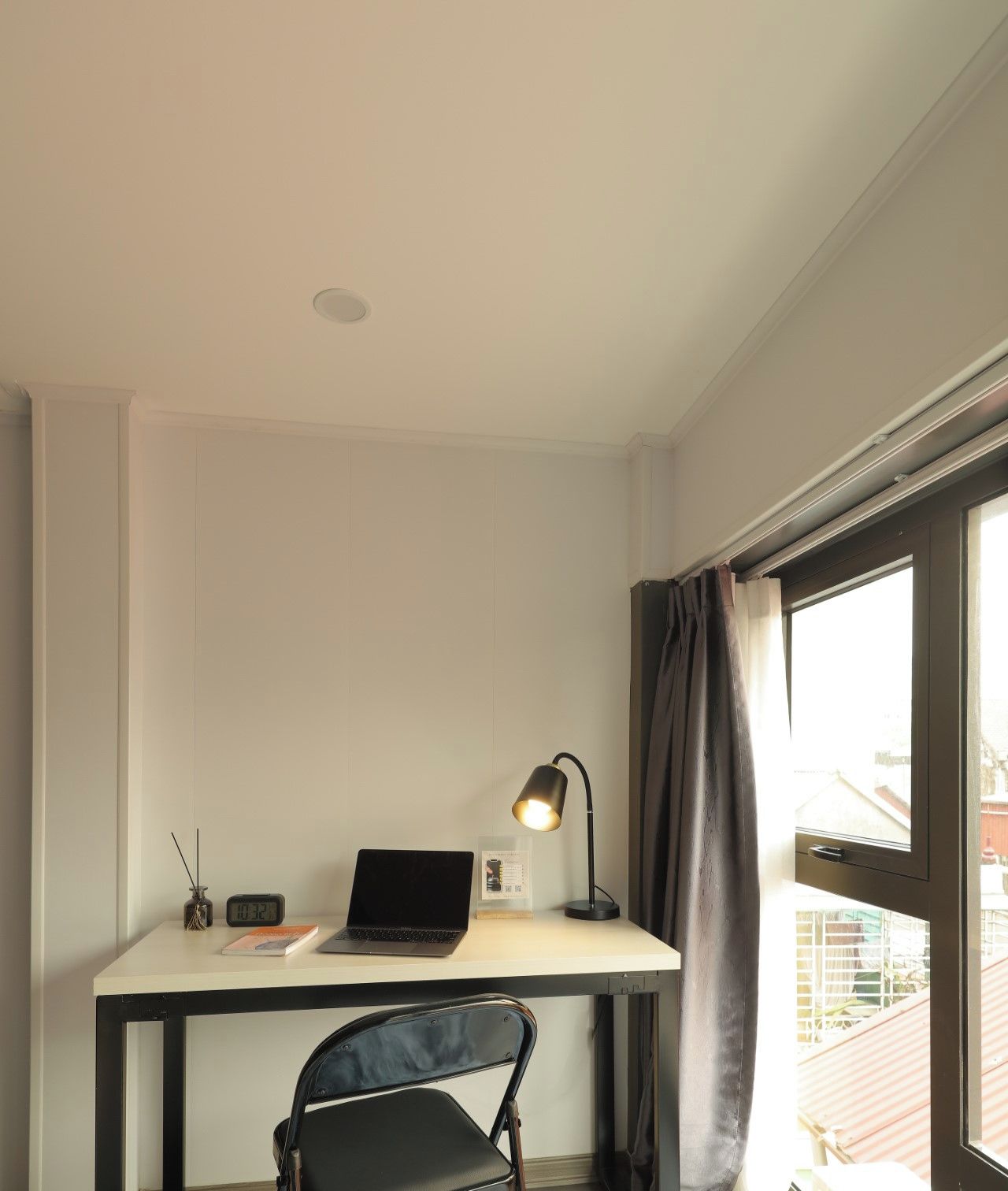 Une chambre moderne équipée d’un bureau, d’une chaise, d’un ordinateur portable, d’une lampe et offrant une vue sur l’extérieur.