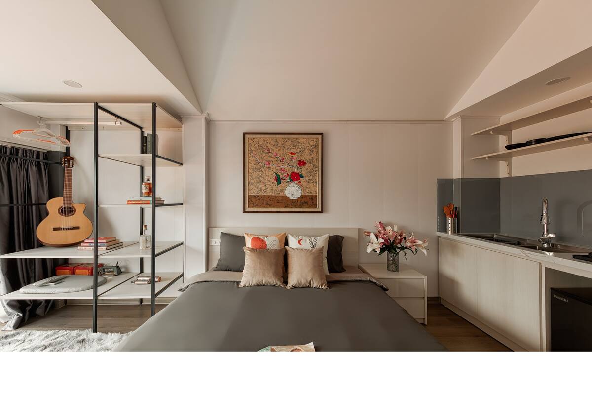 A modern bedroom with a bed, a TV, a guitar, and a bookshelf.