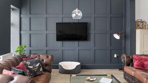 A living room with a dark grey paneled wall, a mounted flat-screen TV, leather sofas, a glass coffee table, and a hanging pendant light. - Stylish Apartment with Parking, Central Ilfracombe (Ilfracombe)