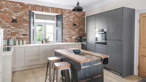 A kitchen with a brick wall, a large island with stools, a refrigerator, and a window with a view. - Stylish Apartment with Parking, Central Ilfracombe (Ilfracombe)