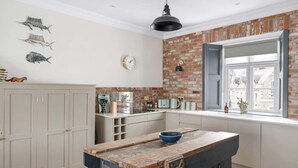 A kitchen with a brick wall, a large window, and a rustic island. - Stylish Apartment with Parking, Central Ilfracombe (Ilfracombe)