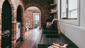 A kitchen with brick walls, a black countertop, and a wooden cutting board with vegetables. - Wandarra Homestead | Luxury Country Retreat (Lue)