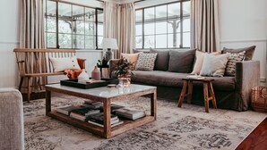A cozy living room with a sofa, coffee table, and a window with curtains. - Wandarra Homestead | Luxury Country Retreat (Lue)