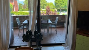 Habitación con puerta de vidrio corrediza que da a un patio al aire libre. El patio tiene una mesa y sillas, y se ven dos mancuernas en el suelo.