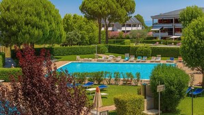 Una piscina con sillones de descanso, rodeada de setos y árboles bien cuidados.