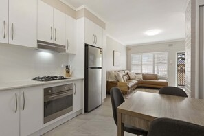 Une cuisine moderne avec des meubles blancs, un réfrigérateur en acier inoxydable et un coin repas comprenant une table et des chaises en bois.