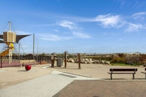 Une promenade en bord de mer avec un banc, une sculpture sphérique rouge et une clôture en métal.