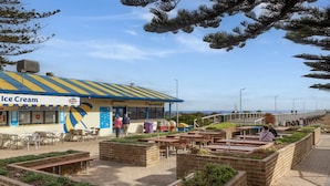 An outdoor seating area with tables and chairs, a building labeled 'Ice Cream,' and a view of the beach.