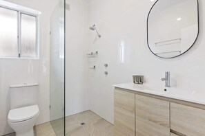 Ein Badezimmer mit Duschkabine, Toilette, Waschbecken mit Spiegel und Holzschränken.