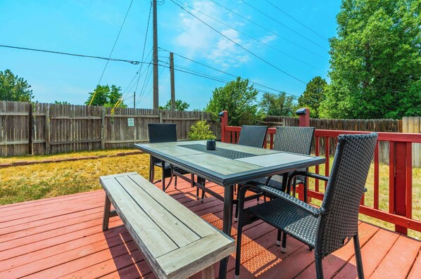 A wooden deck with a table and chairs, a bench, and a red railing.