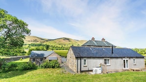 A stone house with a sloped roof, a small attached shed, and a grassy yard.