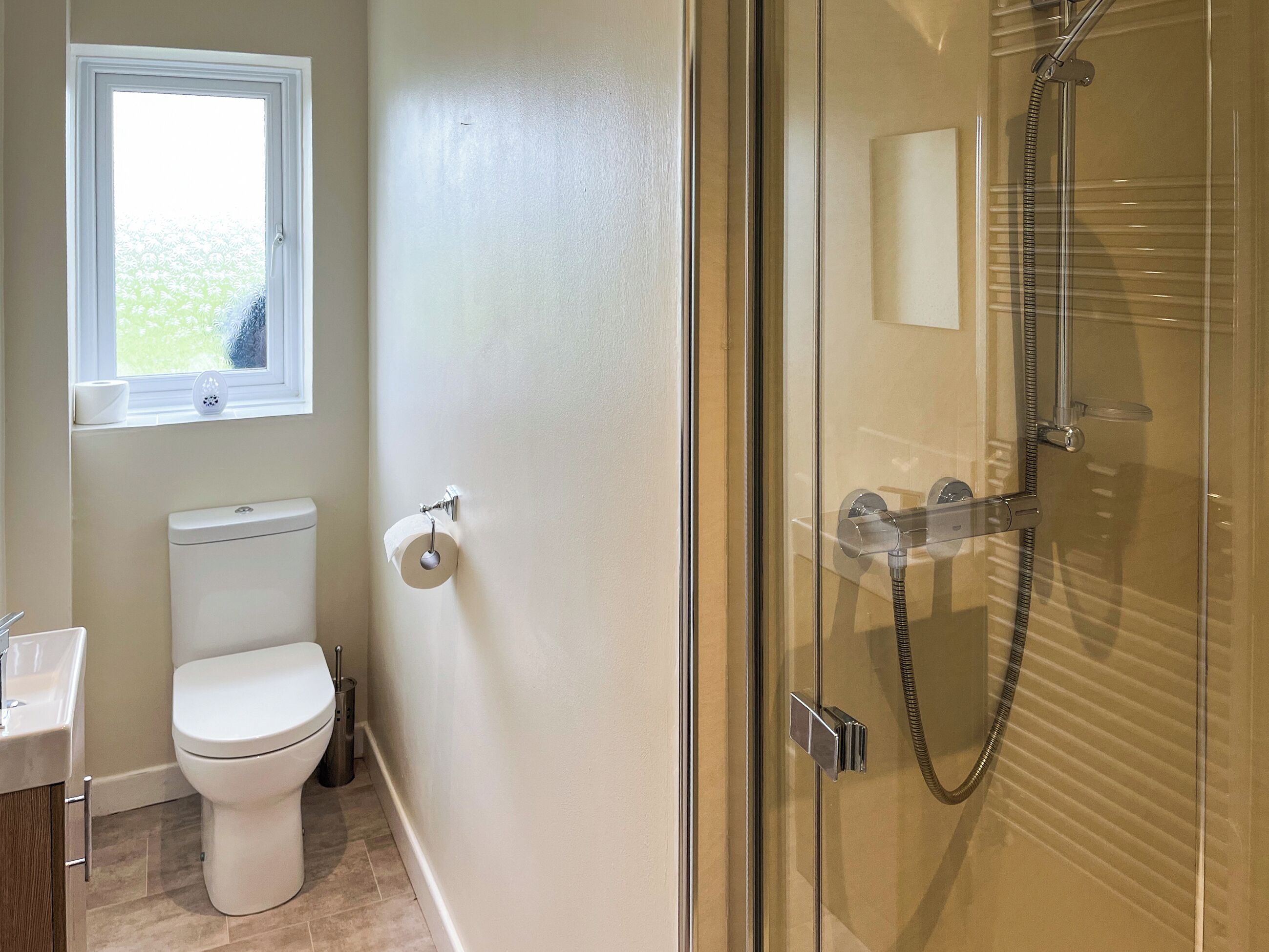 Et badeværelse med toilet, et vindue og en brusekabine med glasvægge.