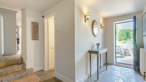 Ein Flur mit Treppe, einer Tür, einem Wandspiegel und einem kleinen Tisch mit einer Vase.