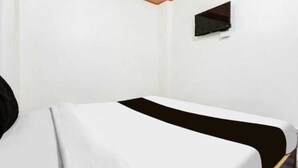 A hotel room with a bed, a small window, and a wall-mounted TV. - Shri Yamuna Dham (Mathura)