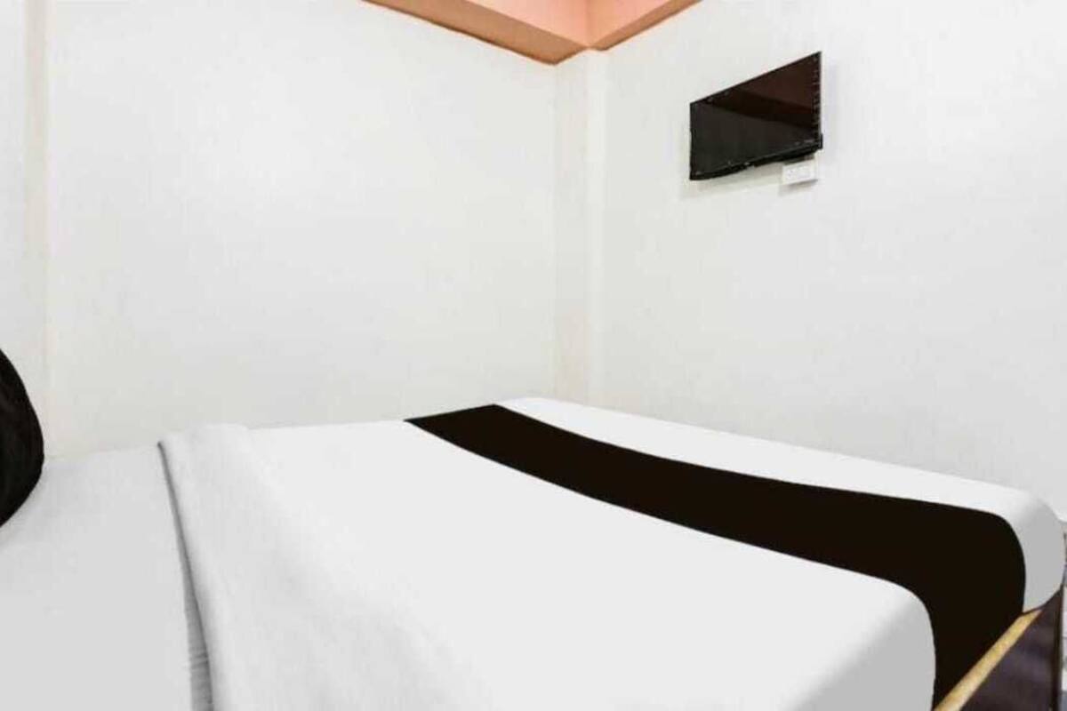 A hotel room with a bed, a small window, and a wall-mounted TV.