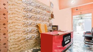 A hotel reception area with a red counter, a decorative wall, and a view of the outside. - Shri Yamuna Dham (Mathura)