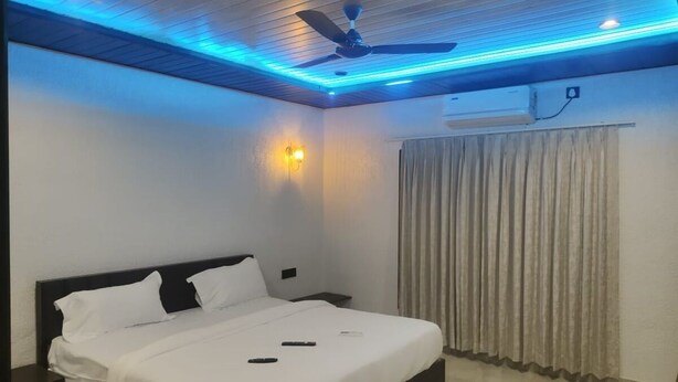 A bedroom with a bed, ceiling fan, wall-mounted air conditioner, and a window with curtains. - Madhurai Resort (Chikhaldara)