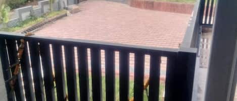 A rooftop terrace with a brick floor, surrounded by a low stone wall and a metal railing.