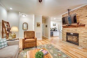 A living room with a fireplace, a television mounted above it, a sofa, a chair, and a coffee table with a magazine and plant.