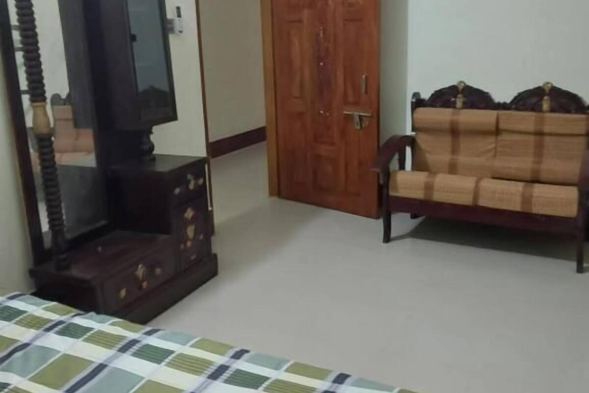 A bedroom with a bed, a wooden wardrobe, a wooden door, and a sofa.