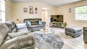 Un salon avec un canapé en cuir, une table basse en verre et un pouf gris.