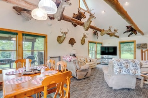 Un salon spacieux avec une grande table à manger en bois, des sièges confortables et une tête de cerf fixée au mur.