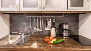 A kitchen with a stainless steel sink, a microwave, a coffee maker, and various utensils hanging on the wall.