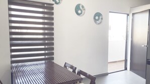 A dining area with a wooden table and chairs, a window with blinds, and three decorative wall pieces. - Roma Suite A Malecon of Mazatlan (Mazatlan)