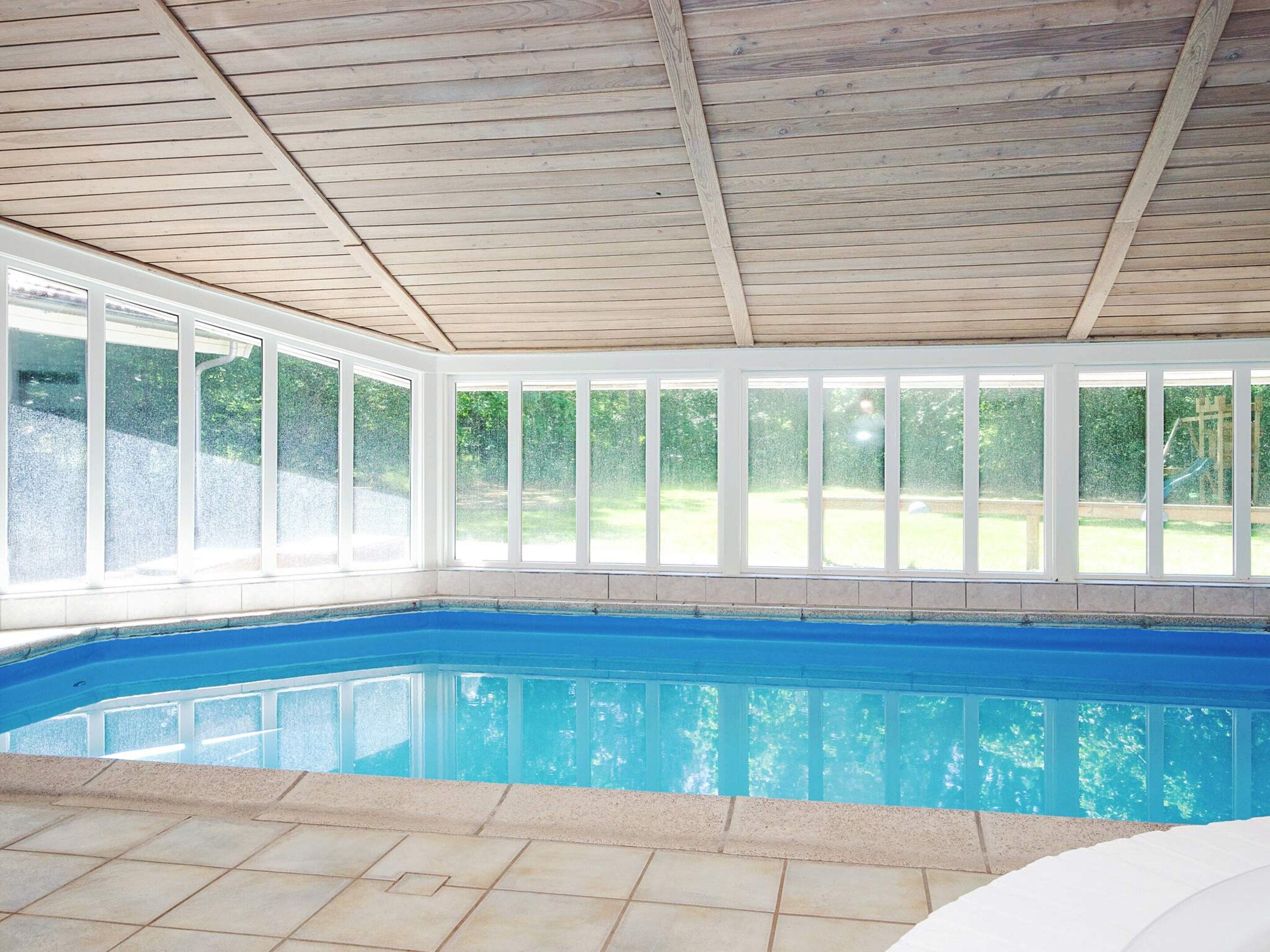 Una piscina interior con techo de madera y ventanas amplias.