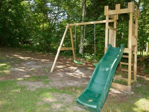 A wooden swing set with a green slide in a wooded park area. - 4 Star Holiday Home in Vig (Vig)