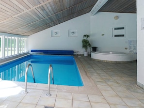 En indendørs swimmingpool med blå vand, en blå bænk, et spabad og en potteplante.