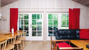 Ein gemütliches Zimmer mit einem Holzesstisch, Stühlen, einem schwarzen Ledersofa und großen Fenstern mit roten Vorhängen.