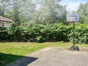 En basketballkurv i en græsplæne med en hæk i baggrunden.