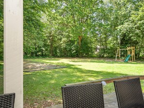 A backyard with a wooden swing set and a green slide, surrounded by trees and a grassy lawn. - 4 Star Holiday Home in Vig (Vig)