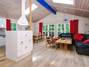 A spacious living area with a wooden floor, a black leather sofa, a wooden dining table, and red curtains. - 4 Star Holiday Home in Vig (Vig)