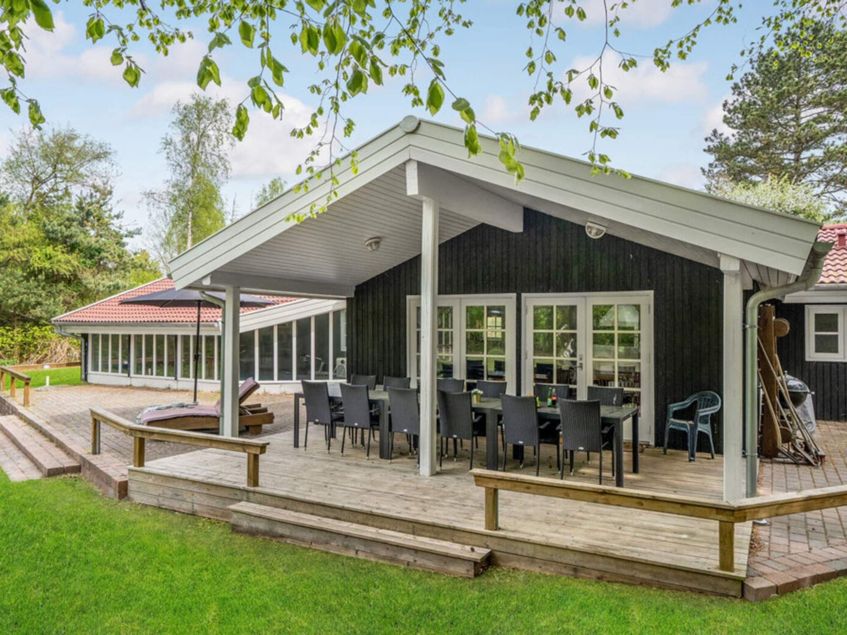 Un espace extérieur aménagé, abrité et doté de tables et de chaises, d’une terrasse en bois et d’une vue sur un bâtiment dont le toit est recouvert de tuiles rouges.