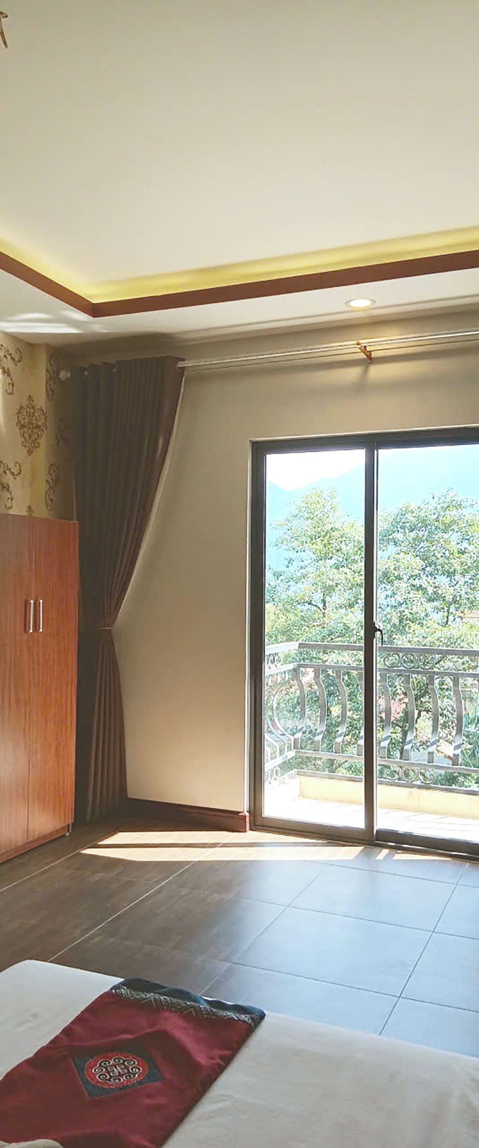 A hotel room with a large sliding glass door leading to a balcony with a view of trees and a railing.
