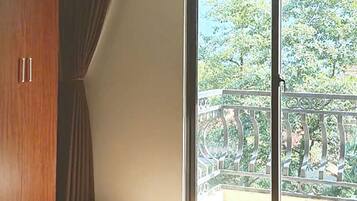 A hotel room with a large sliding glass door leading to a balcony with a view of trees and a railing.