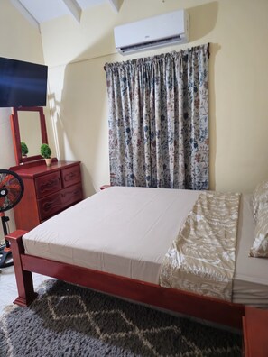 A bedroom with a bed, a dresser, a mirror, a TV, and an air conditioner. - Spacious 3-bedroom apartment with WiFi, AC at amazing Castle Berry (kingstown)