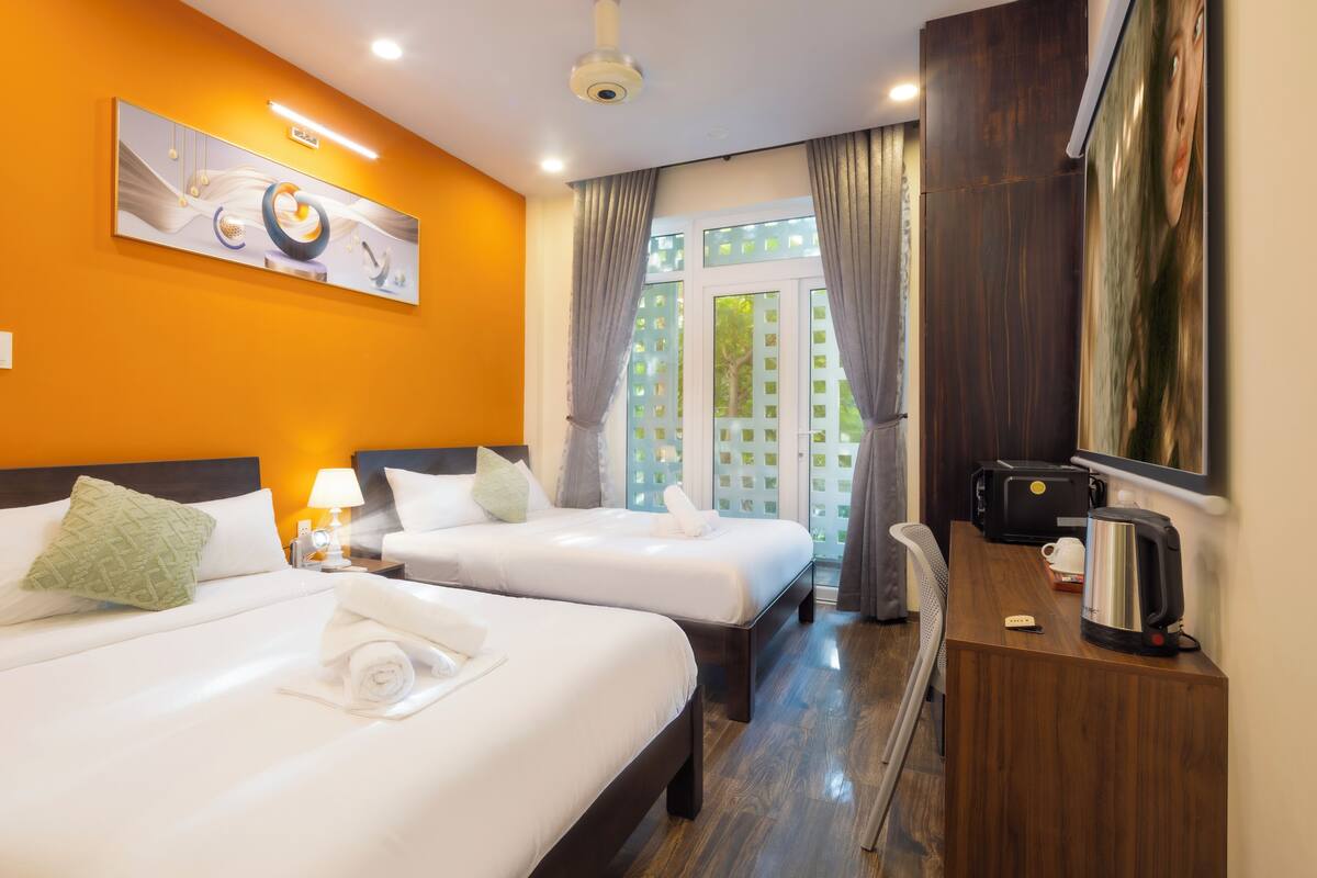 Une chambre d’hôtel avec deux lits, un bureau, une machine à café et une grande fenêtre avec des rideaux.