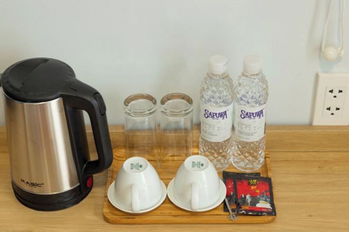 A stainless steel kettle, two glass bottles labeled 'SAPINA', two white cups, and a card on a wooden tray.