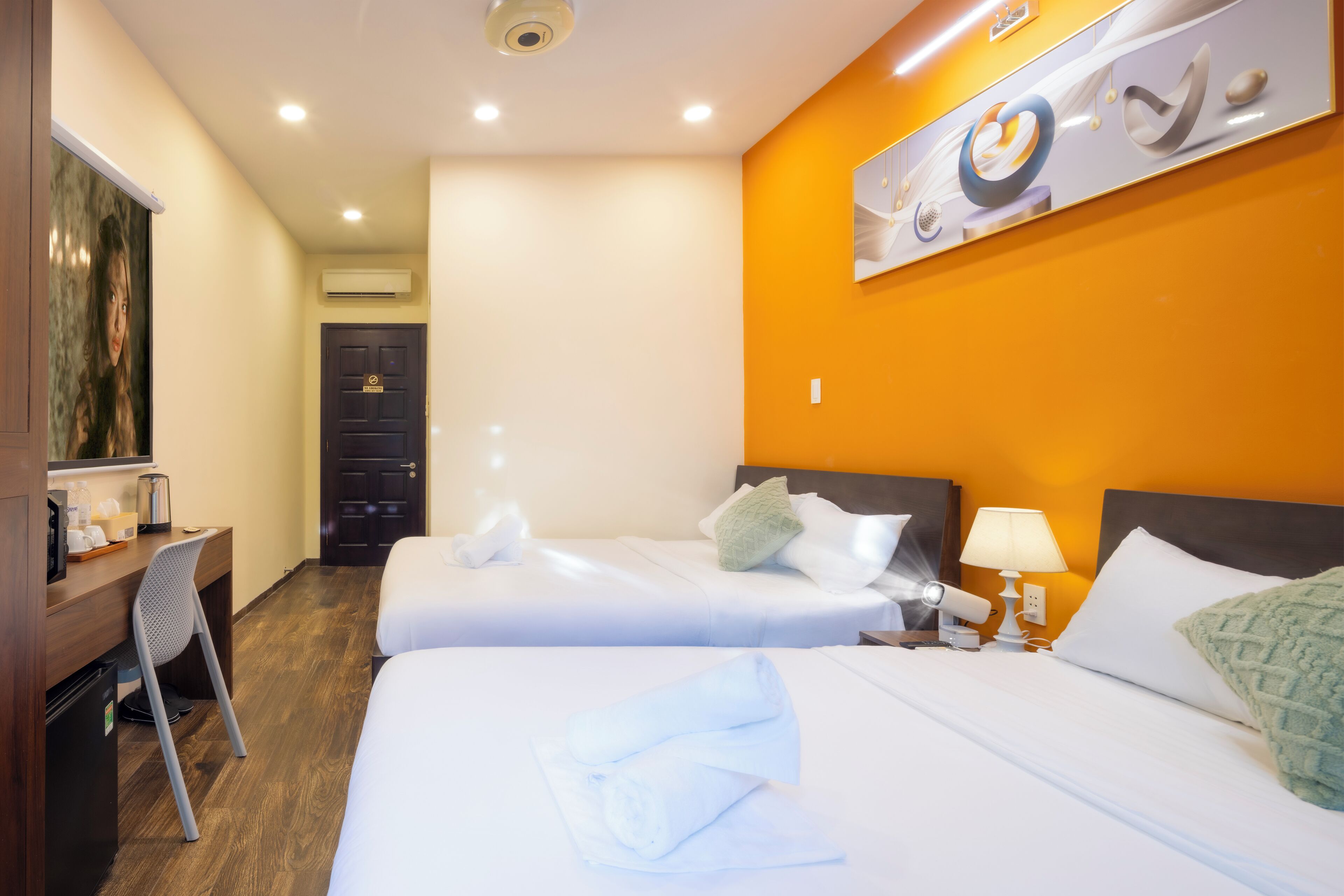 Habitación de hotel con dos camas, un escritorio, una silla y una obra de arte colgada en la pared.
