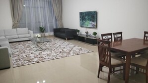 Een moderne woonkamer met een bank, een salontafel, een eettafel met stoelen, een televisie en een groot raam met gordijnen.