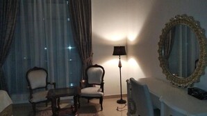 Een kamer met twee fauteuils, een tafeltje, een lamp, een dressoir en een spiegel.